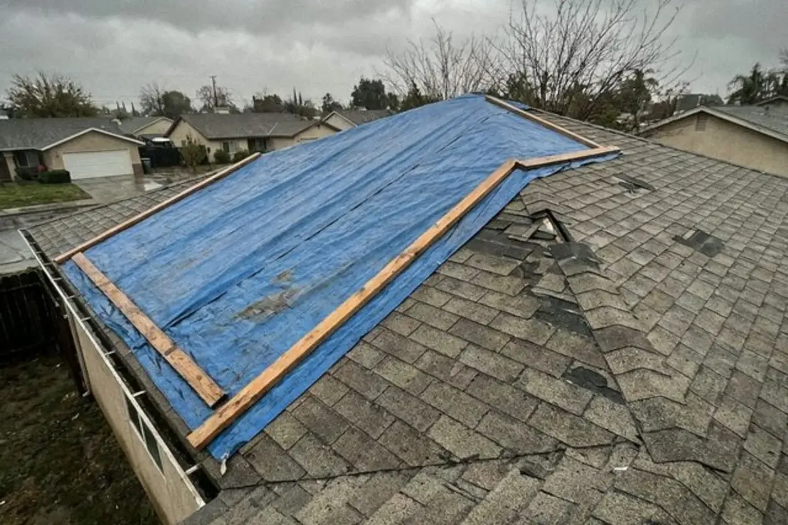Documentary-style iPhone photo of emergency roof tarp installation after storm damage on a residential home in Provo, Utah. Natural lighting.